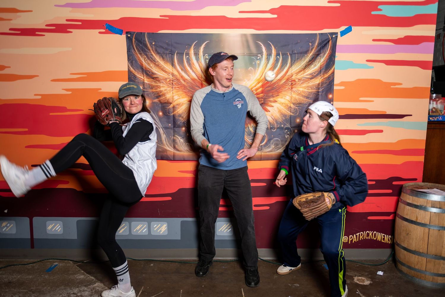 People sit and pose in front of a vibrant orange and red sunset mural painted on a wall.