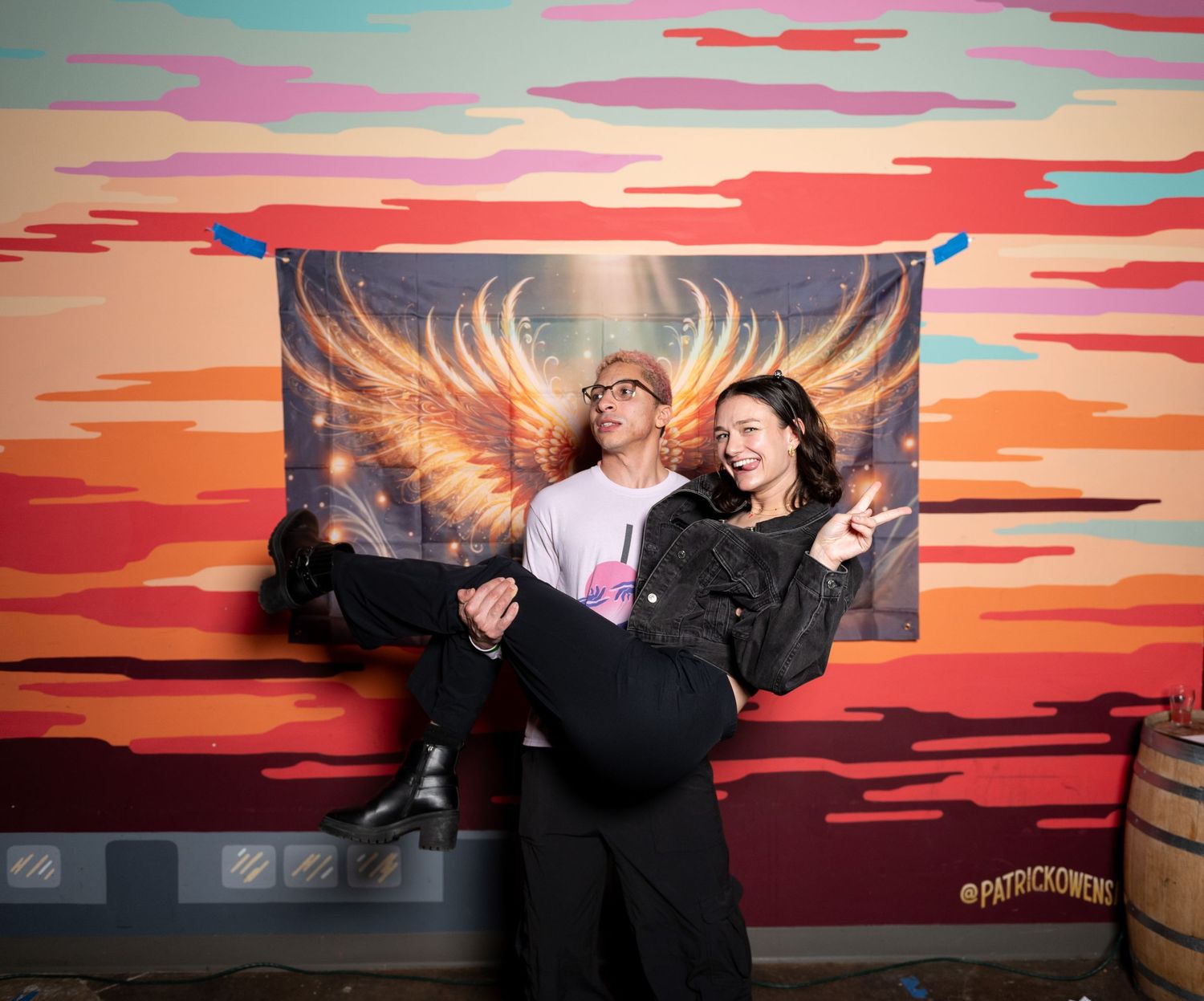Friends strike fun poses against colorful wall art featuring fiery wings and sunset colors.