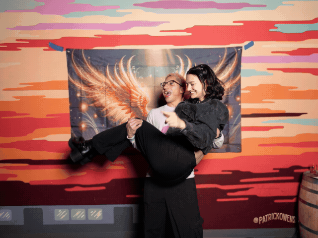 People having fun posing against artistic wall display with illuminated wings.