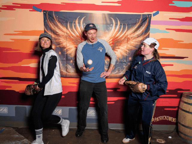People stand in front of a vibrant red and orange wall with artistic cloud designs.