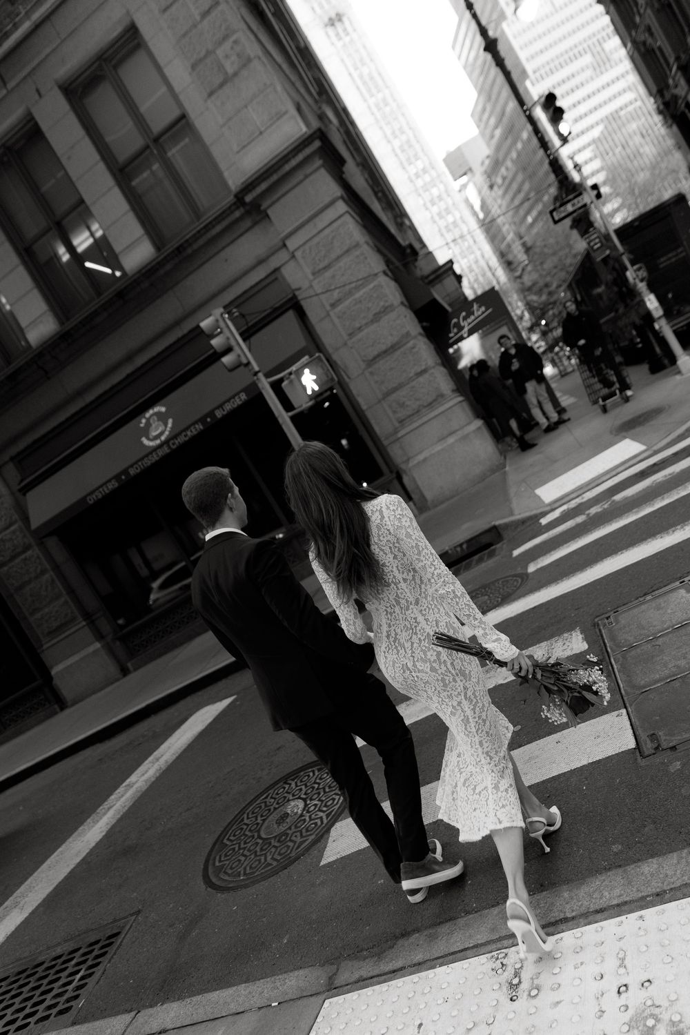 Black and white street scene showing people walking past a building entrance and manhole cover.