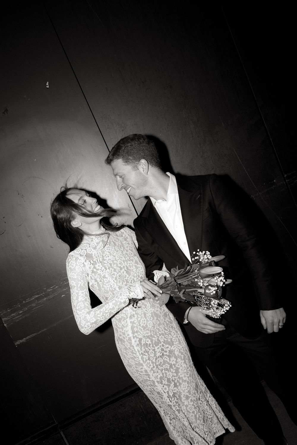 Artistic black and white photo of a couple in formal attire embracing in dramatic lighting.