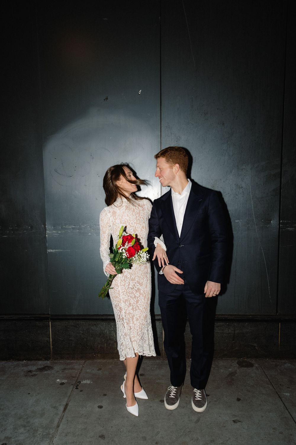 A couple in wedding attire share intimate moments against a dark wall in a series of artistic photos.
