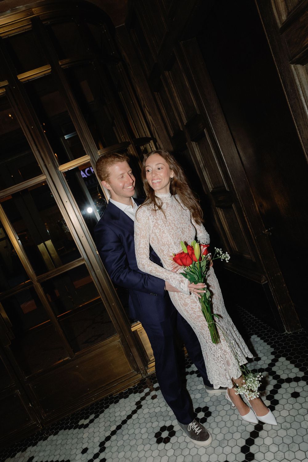 A couple in formal attire dancing together on a tiled floor in a dimly lit indoor space.