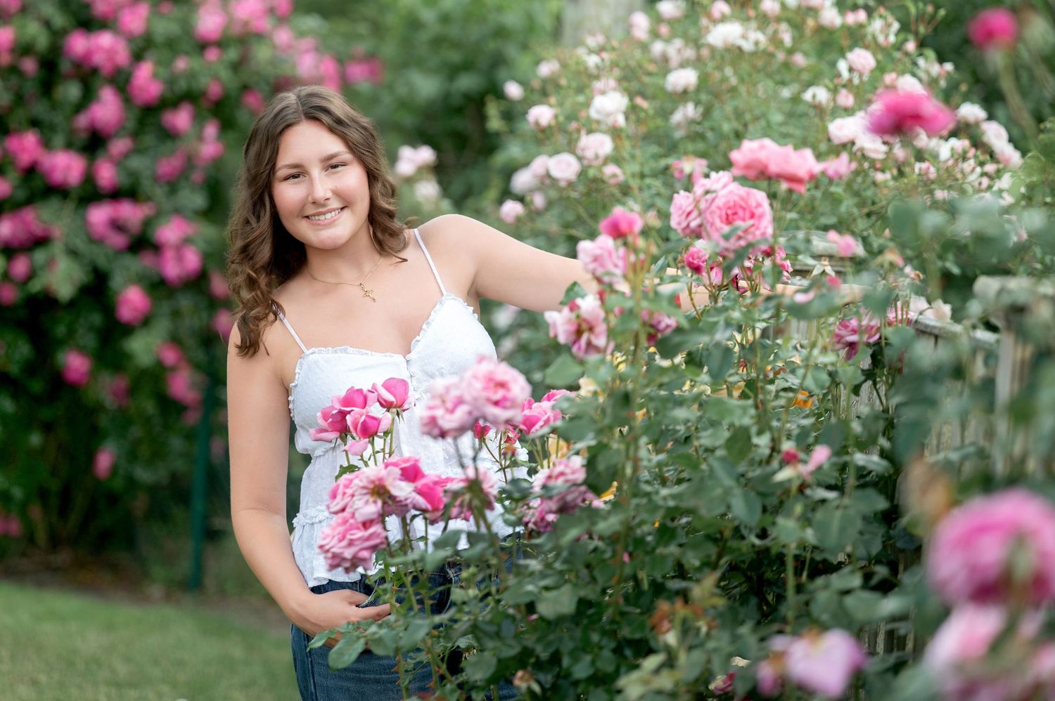 A woman in a yellow dress poses among blooming pink roses in a lush summer garden.
