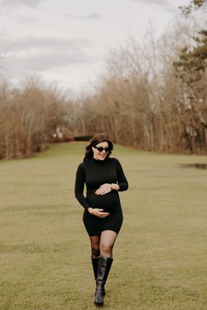 Person in black clothing and boots posing in a grassy field.