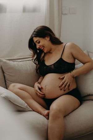 Maternity photo of person relaxing on grey couch in intimate indoor setting.