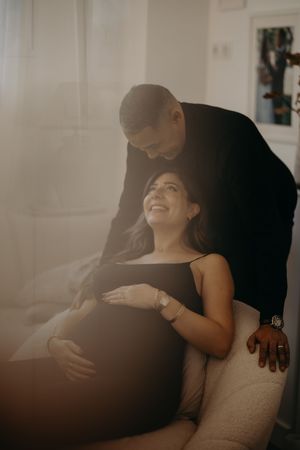 Sunlit maternity photo capturing tender moment between couple in living room.