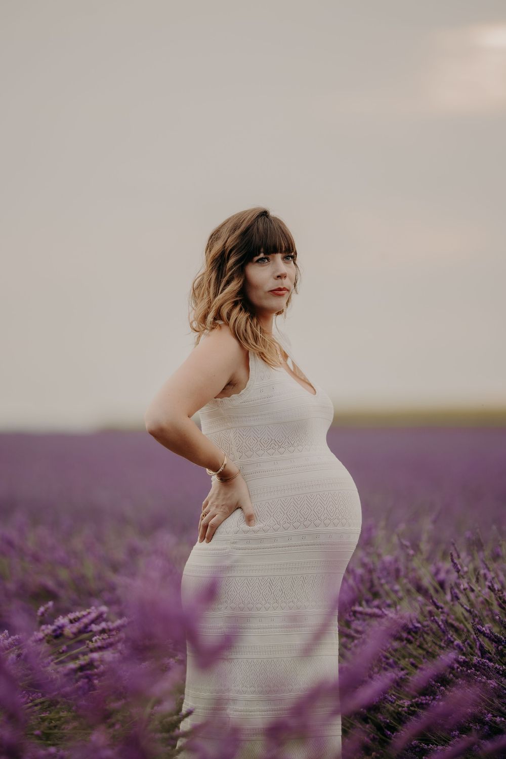 A person in a white dress stands among blooming lavender fields.