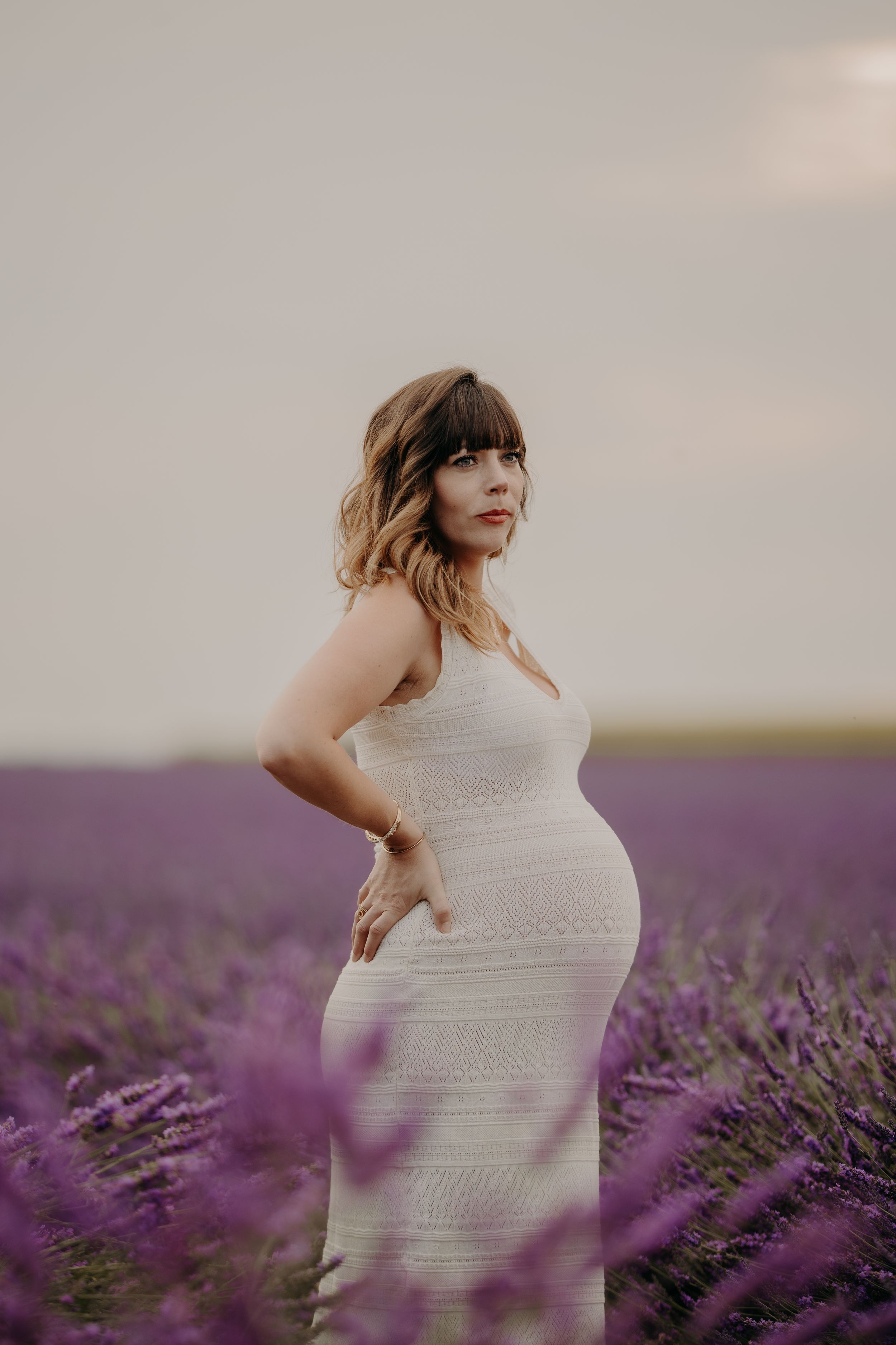 A person in a white dress stands among blooming lavender fields.