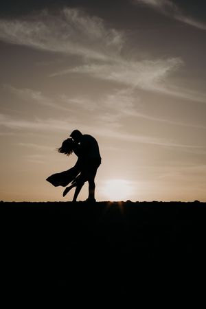 Silhouette of a romantic couple embracing against a dramatic sunset sky.
