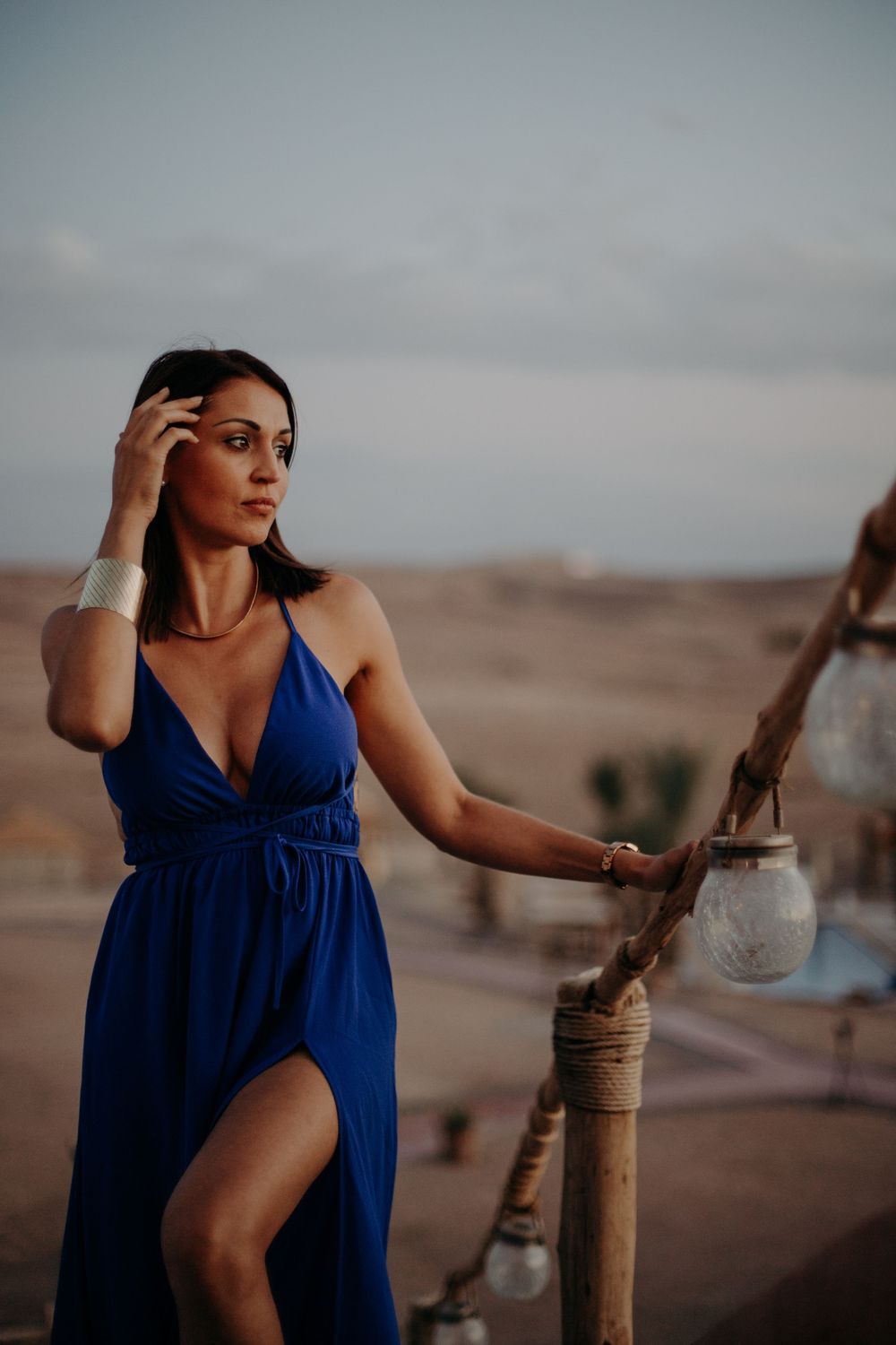 Woman in elegant blue dress poses in desert setting at dusk.