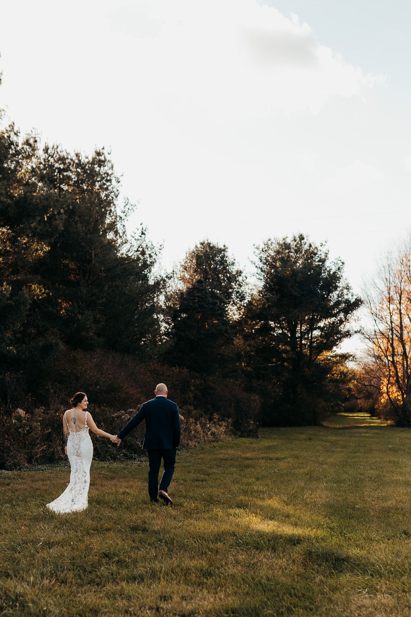 A couple walks together on a forest path surrounded by tall trees during their autumn wedding celebration.