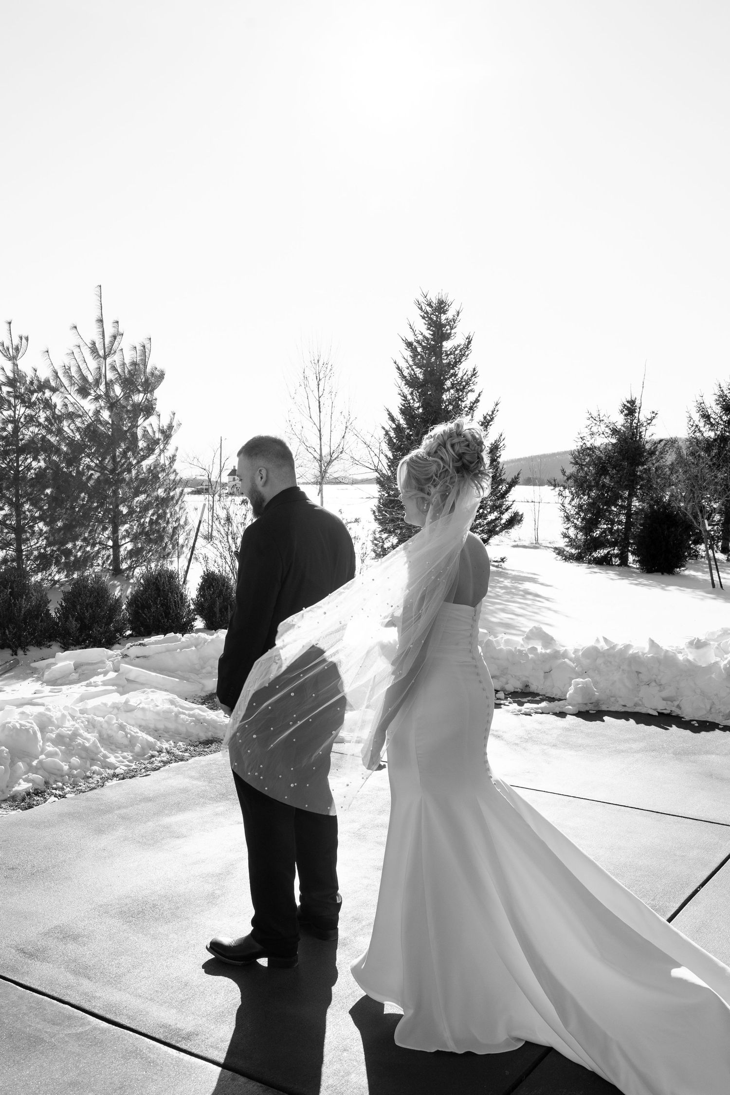 Black and white photo of bride and groom walking together in snowy outdoor winter setting.