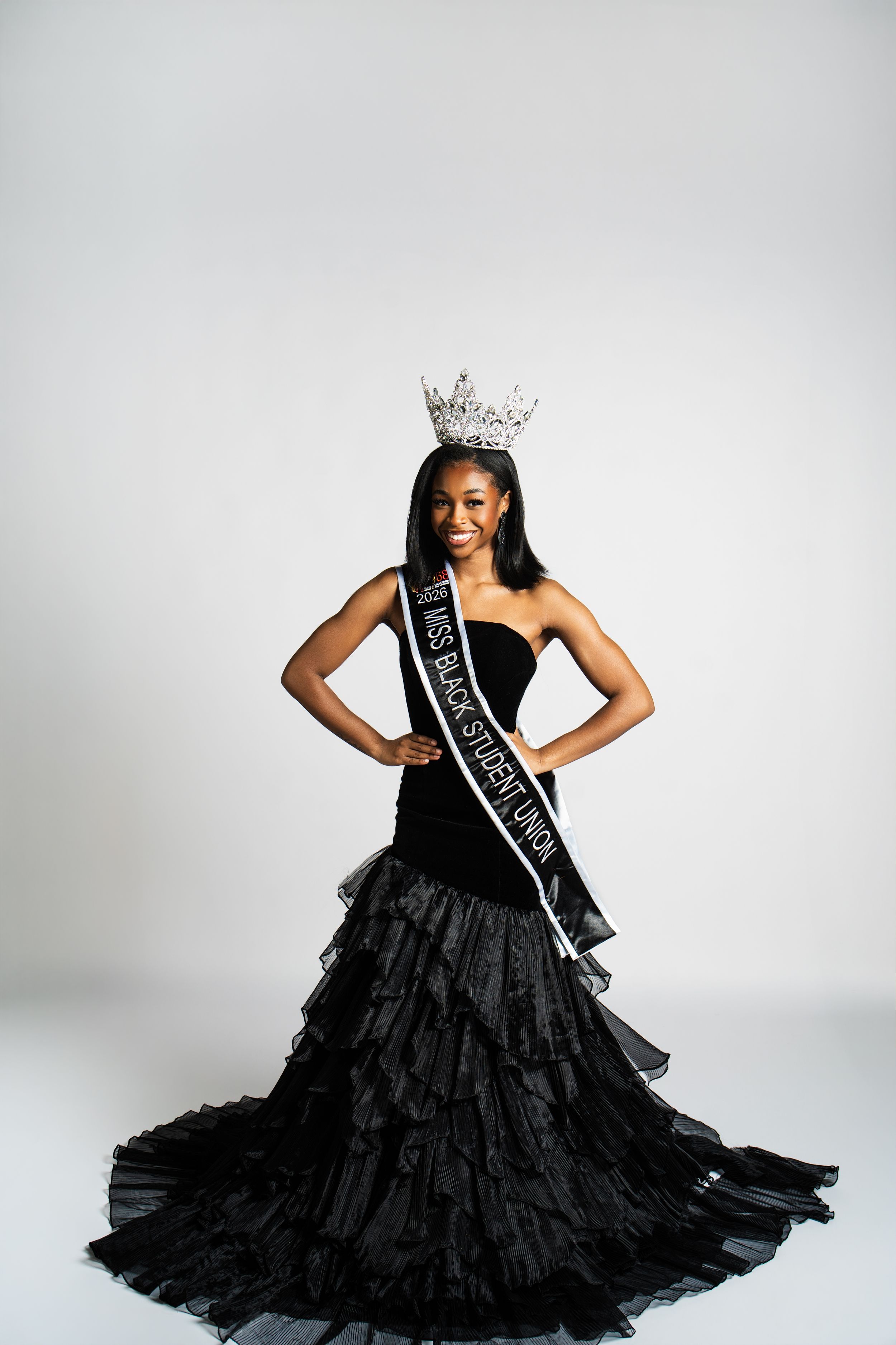 A dramatic black ball gown with ruffled layers swirls during a glamorous photo session against white.