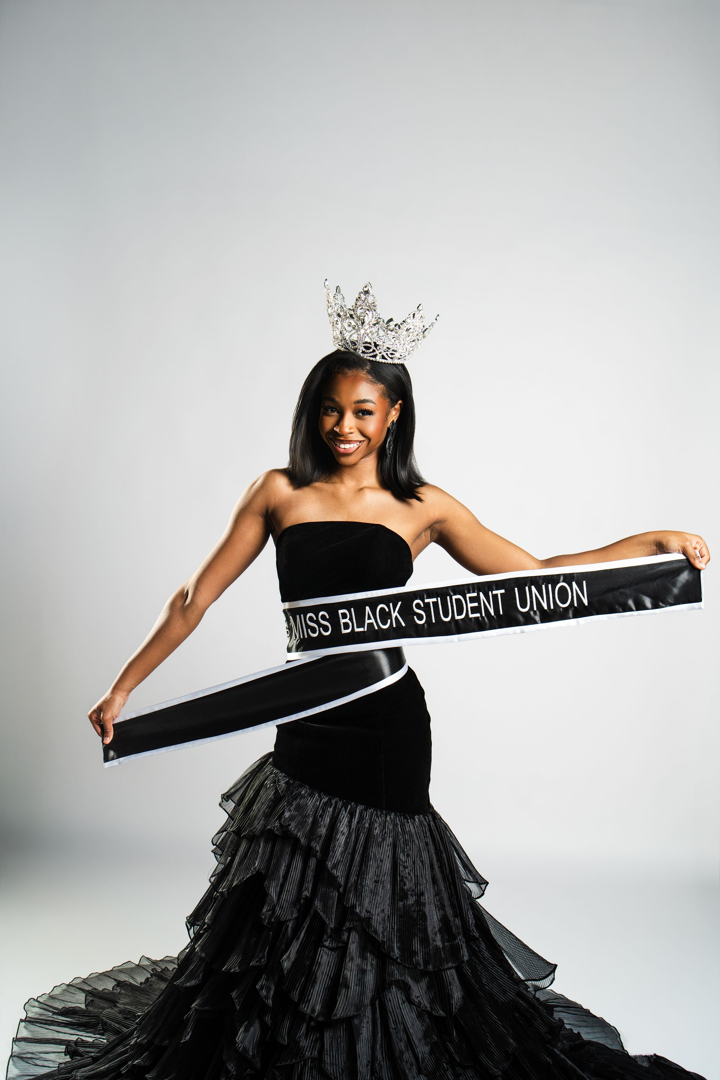 A pageant winner in a black ball gown poses with a sash against a white backdrop in a series of elegant photos.