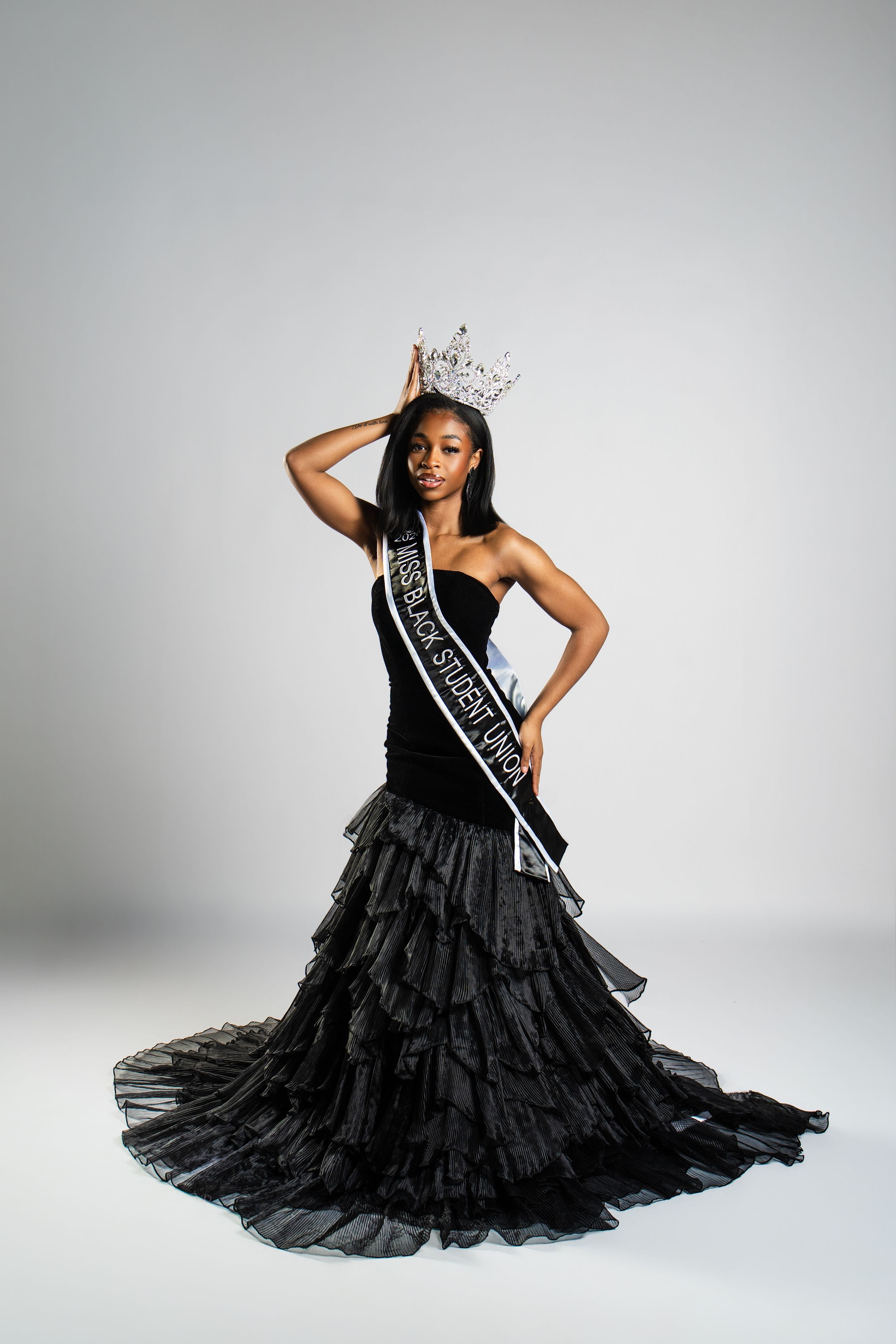 A beauty queen in a dramatic black tulle gown and sash strikes graceful poses during a photo session.