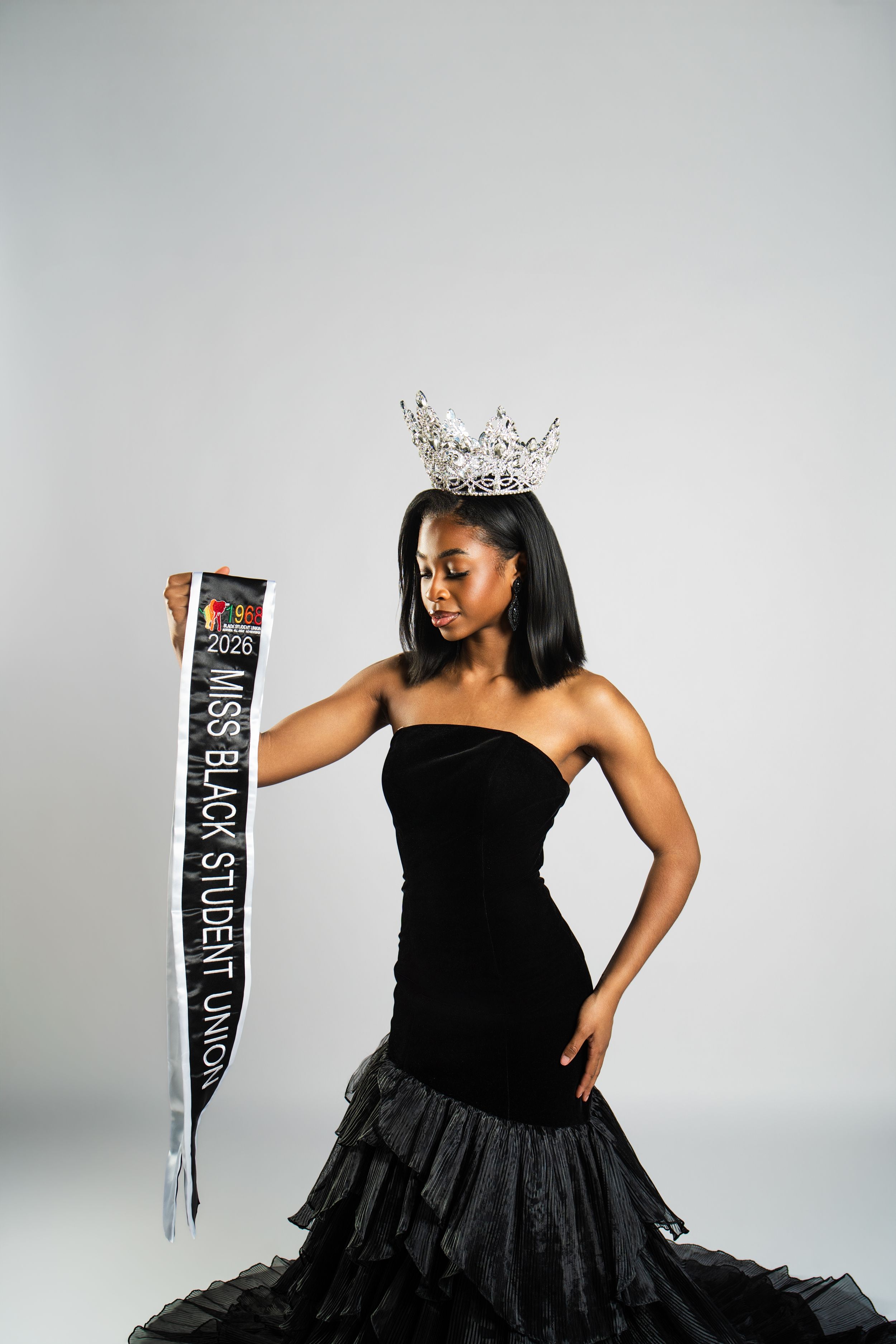 A pageant contestant in a black strapless gown poses elegantly against a light gray backdrop.