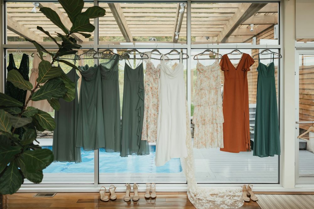 Colorful dresses and garments hanging on a clothing rack against a white wall with natural lighting.