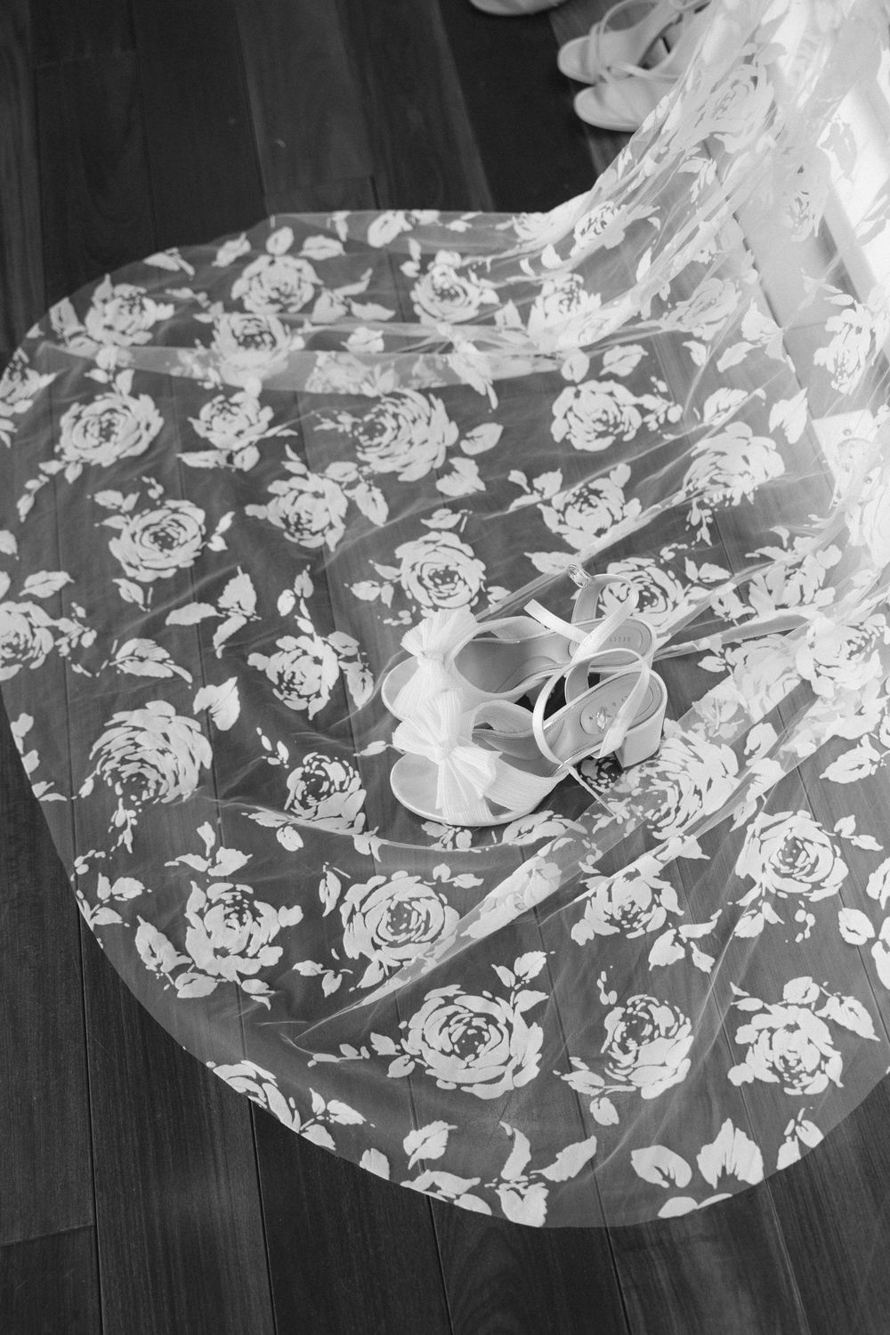 Delicate white floral lace fabric with rose patterns laid out on a dark wooden surface.