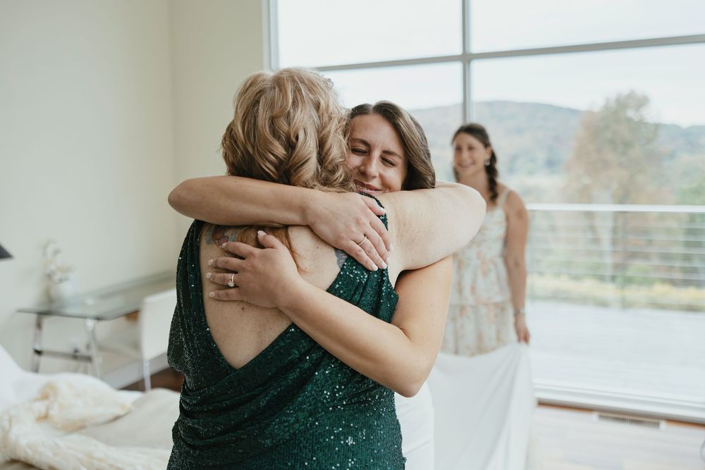 Wedding party members share emotional embraces and moments in a bright indoor venue.