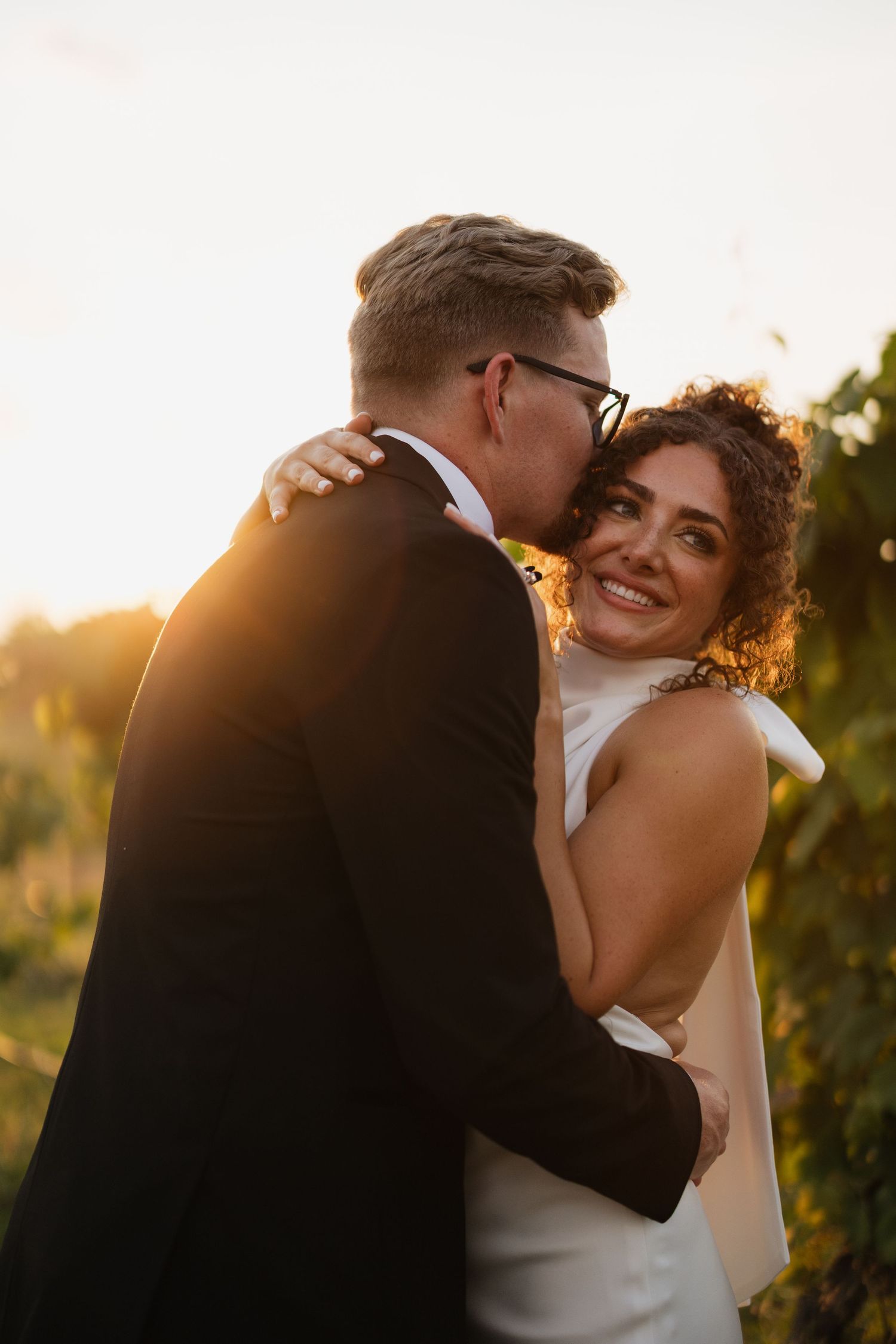 Groom kissing bride on the cheek during a golden hour wedding session at Fair Haven at the Vineyards in Arkansas.