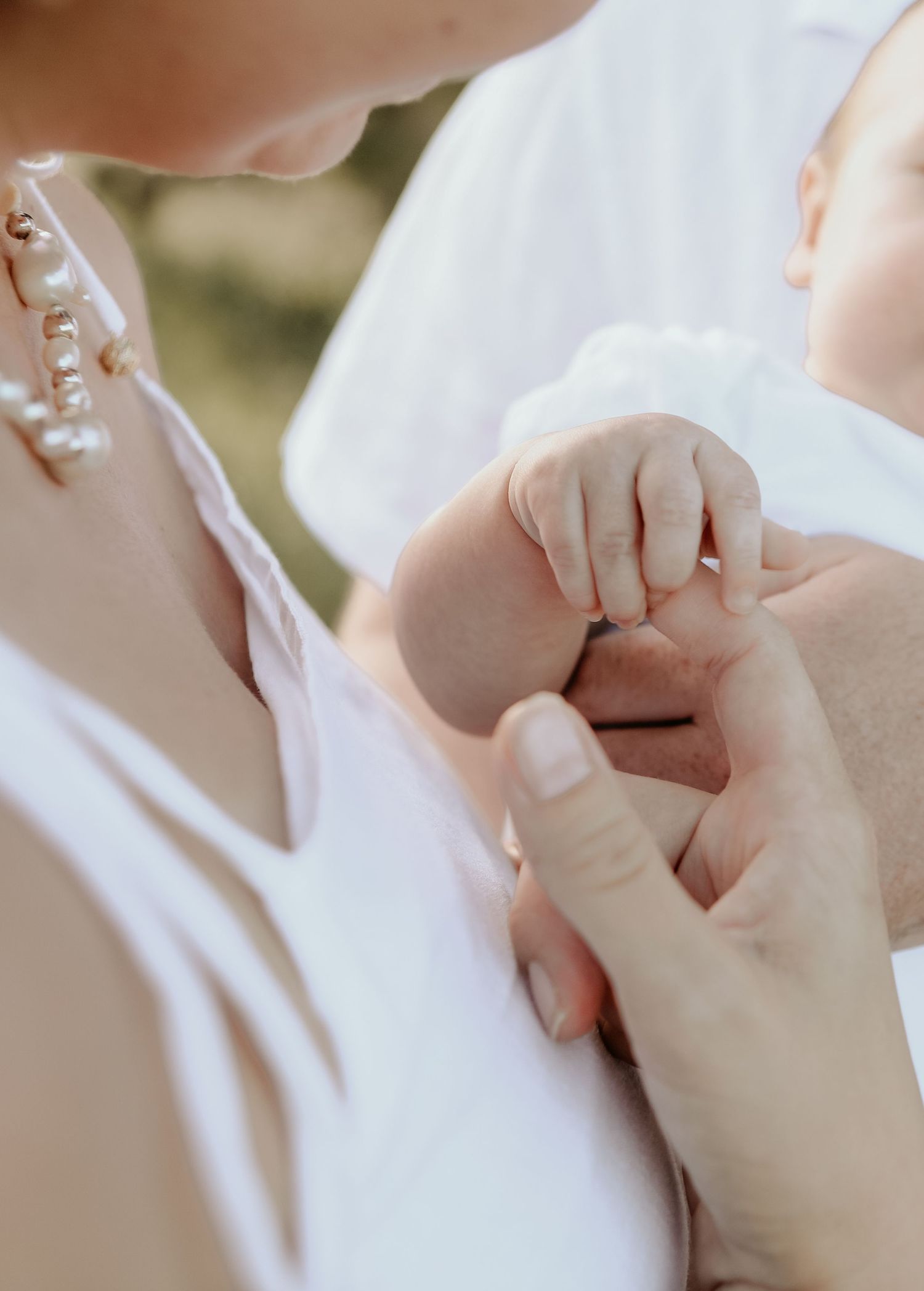 Close-up view of a baby's tiny hand being gently held by an adult hand in soft natural lighting.