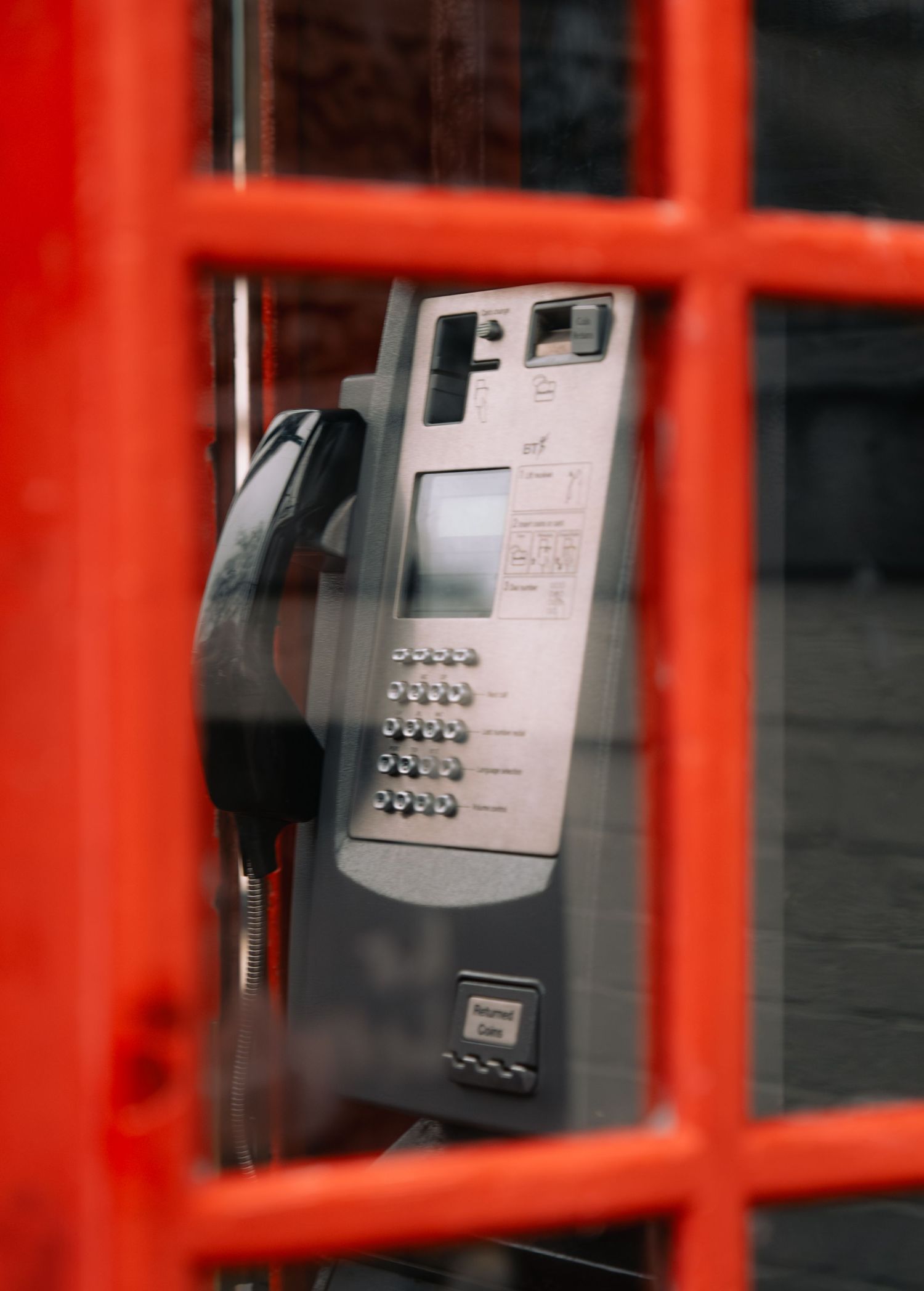 A classic red British telephone box with a modern payphone visible through the glass panels.