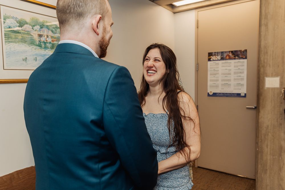 Couple sharing a joyful laugh indoors, woman in blue dress smiling brightly at man in navy suit.
