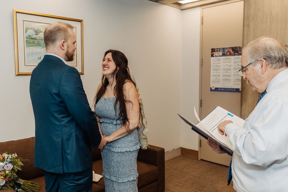 Couple exchanging vows during an intimate civil wedding ceremony with an officiant reading from a book.