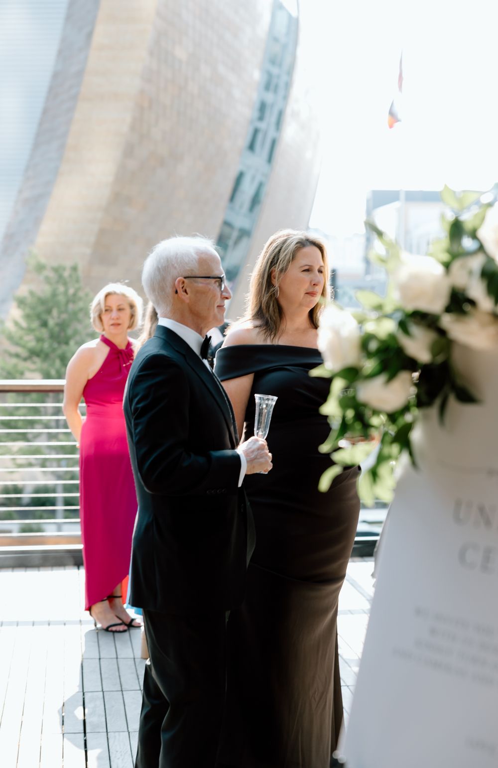 Elegant guests in formal attire mingle on an outdoor terrace during a sophisticated wedding reception.