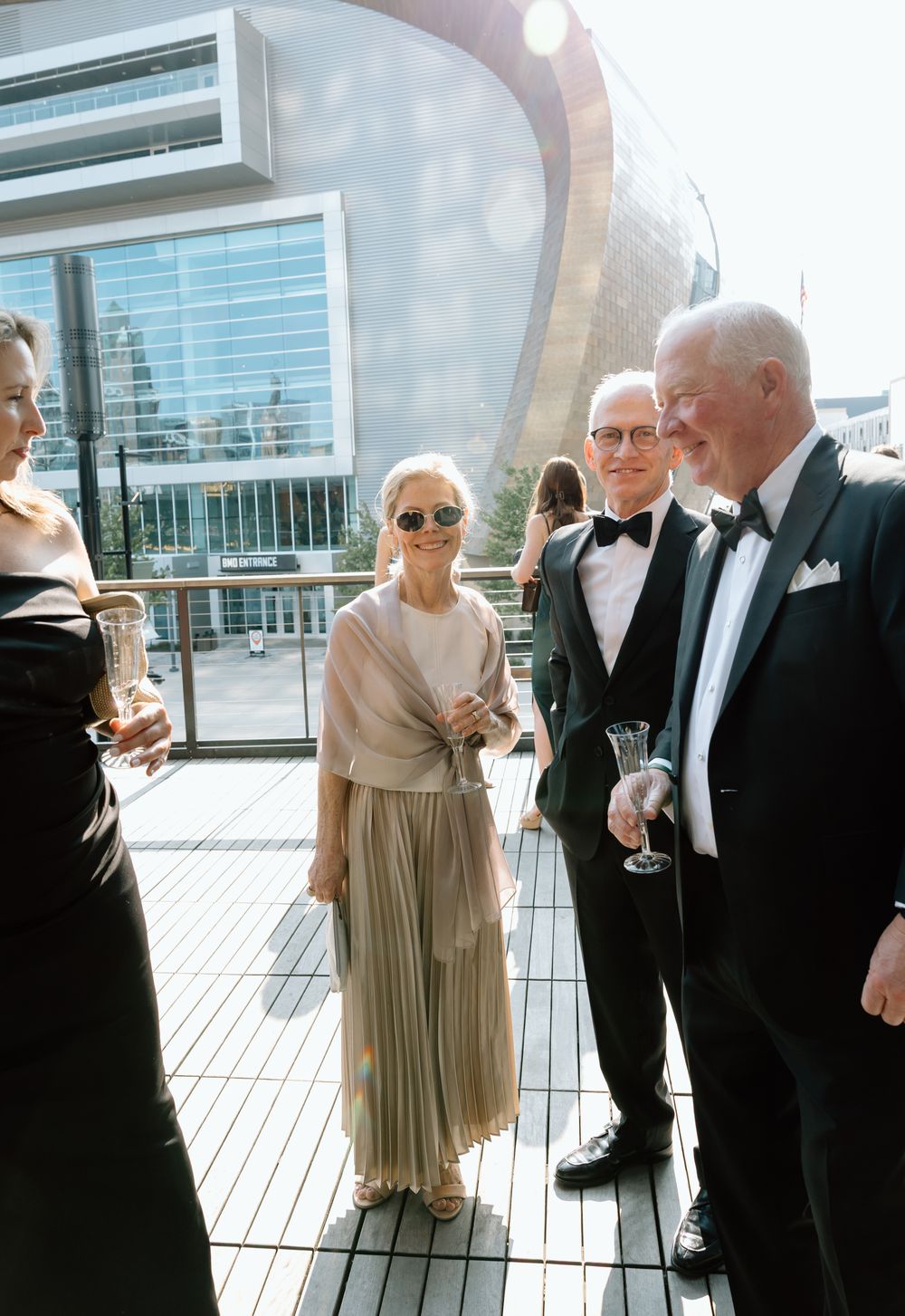 Well-dressed wedding guests in tuxedos and gowns socialize on a modern rooftop venue terrace.