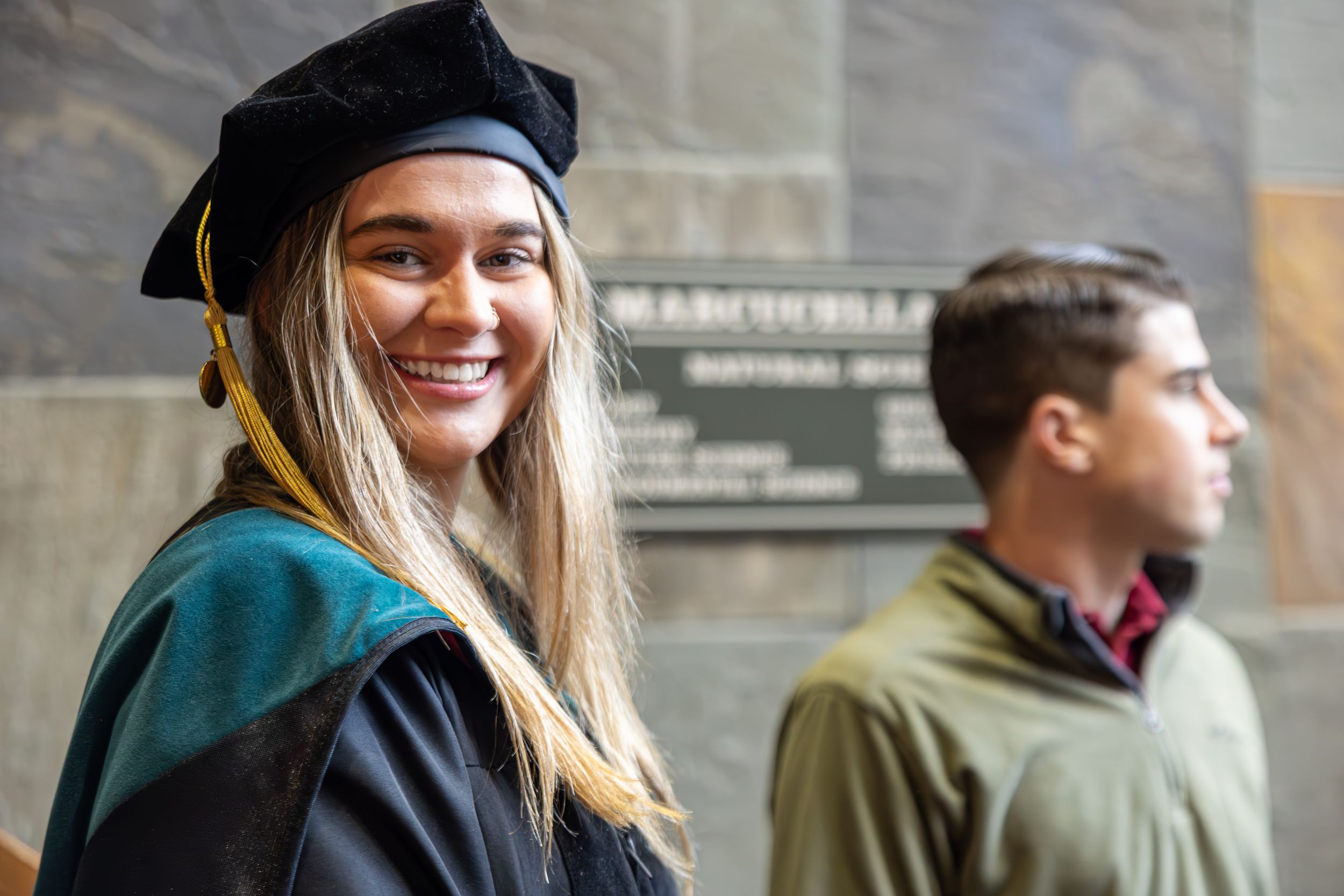 Graduates in traditional academic regalia posing outdoors against stone building.