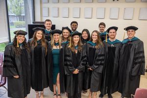 A group of graduates wearing black academic regalia stand together for a photo.