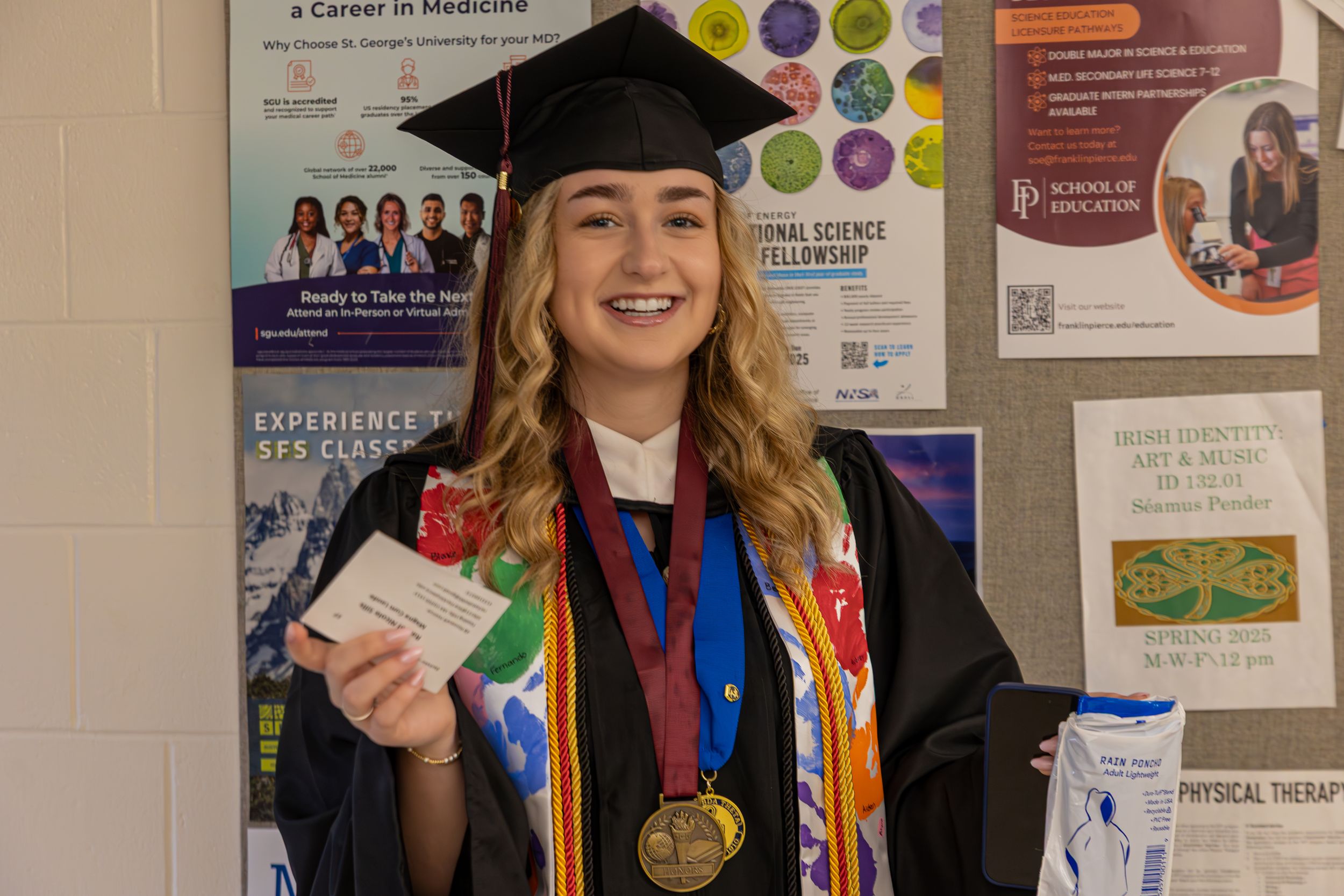 Graduates in academic regalia pose near university posters and displays.