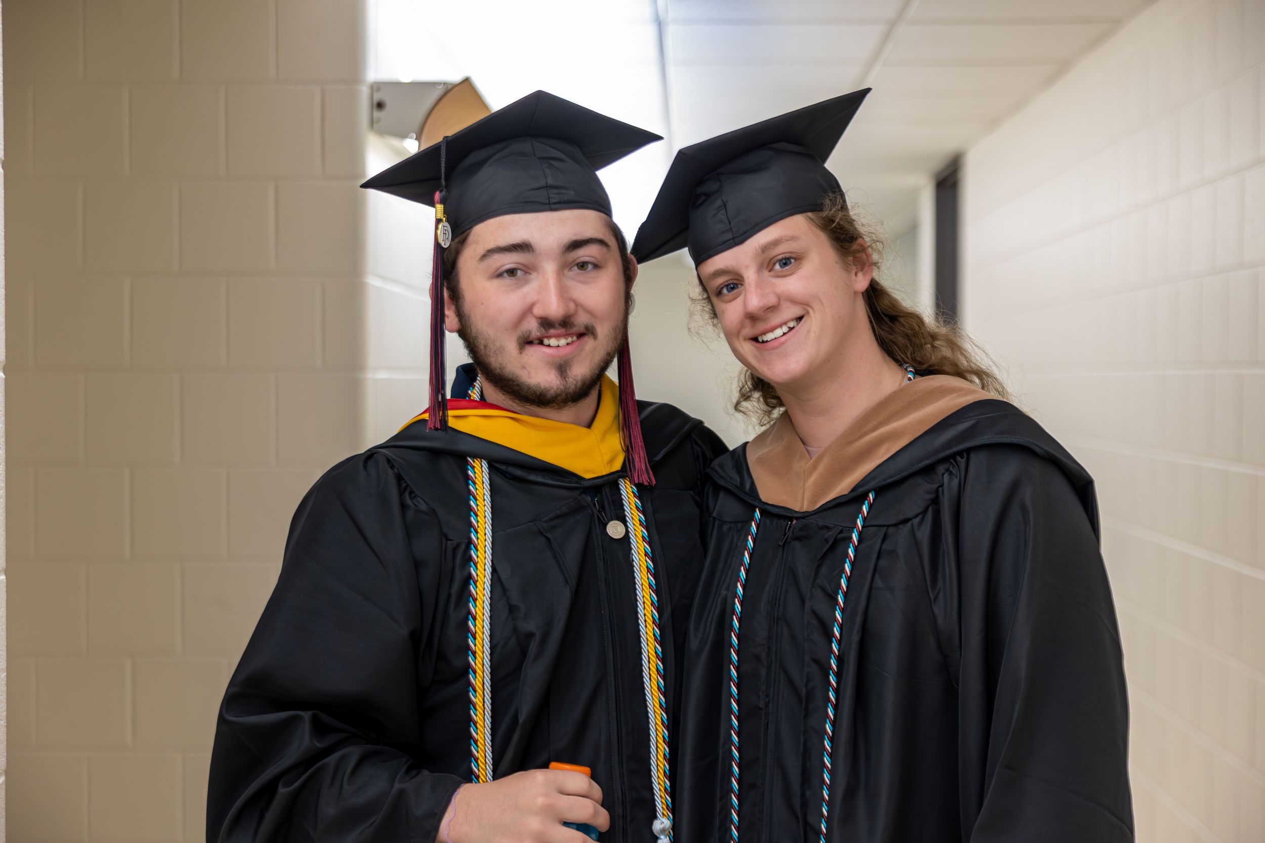 Graduates in black caps and gowns celebrating in hallway.