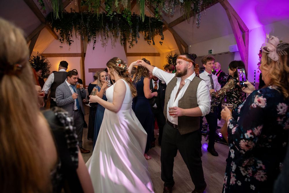 Bride and groom dancing joyfully with wedding guests on a decorated dance floor with purple lighting.