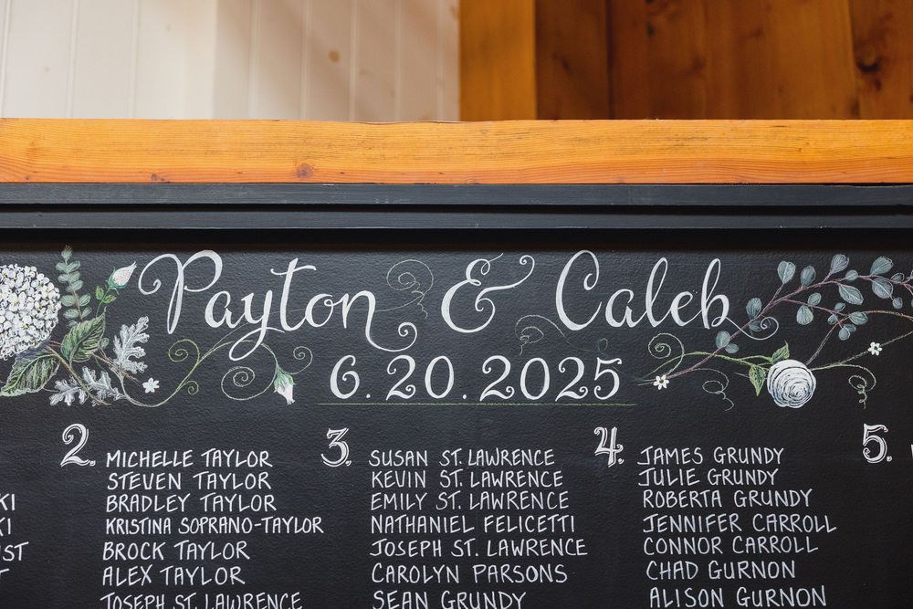 A chalkboard wedding seating chart displays names and table assignments for Payton and Caleb's 2025 wedding.