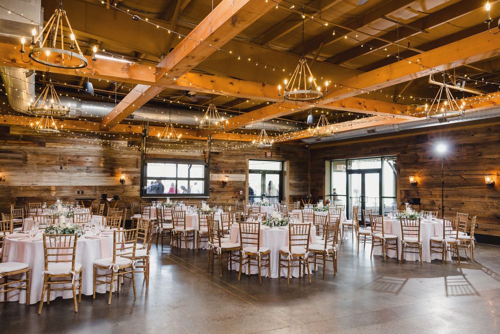 A rustic barn wedding venue with exposed wooden beams and twinkling string lights overhead.