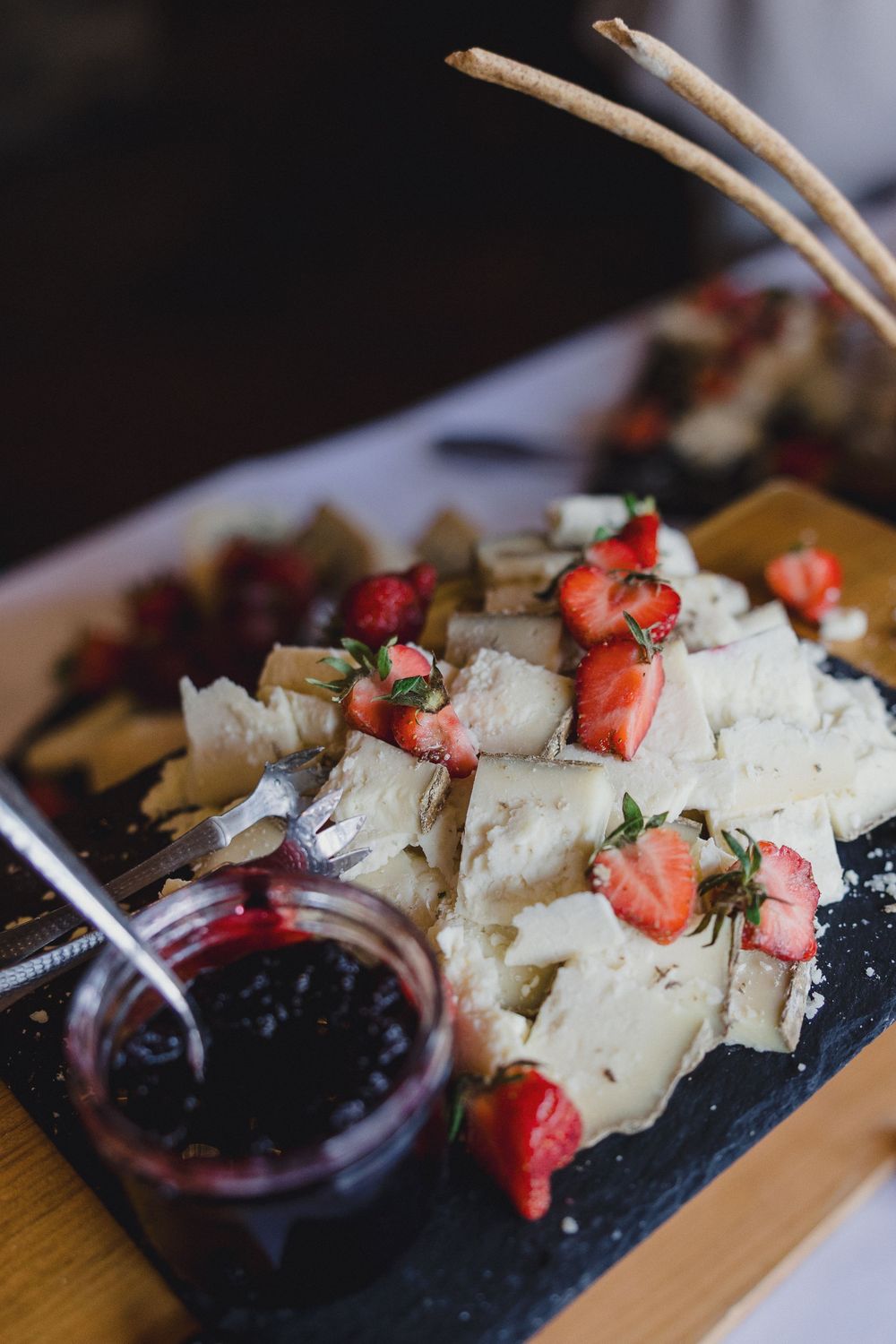 Gourmet cheese board with fresh strawberries and berry compote served on dark slate platter.