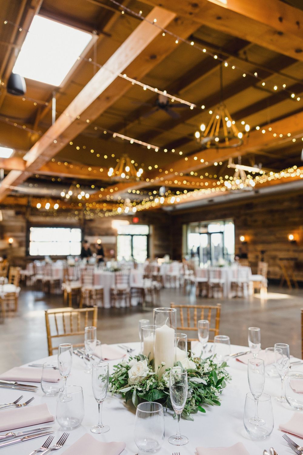 Elegant wedding reception venue with rustic wooden beams and twinkling string lights illuminating white table settings.