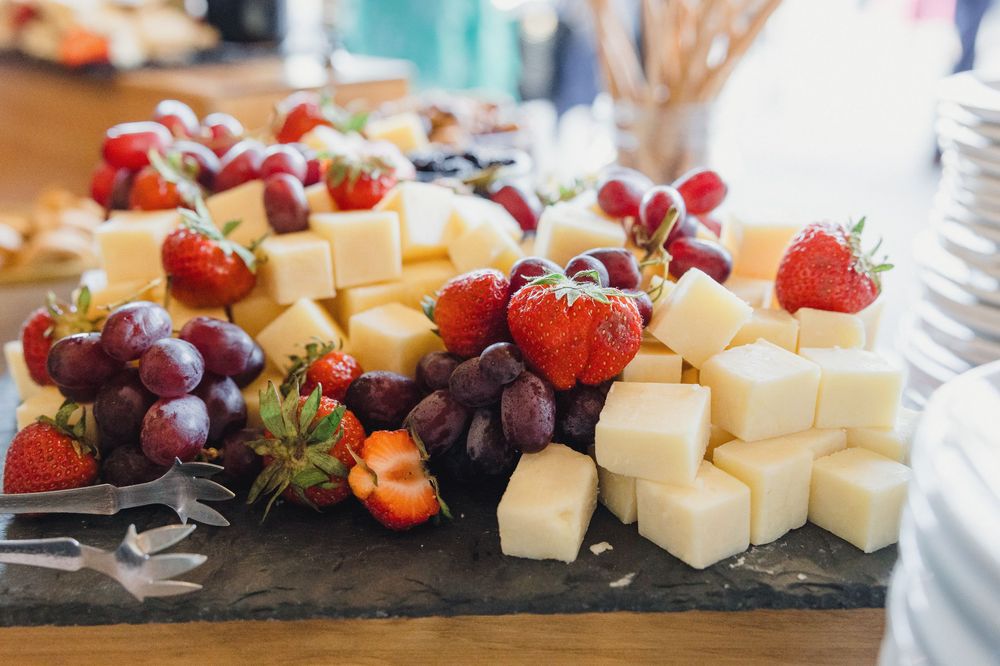 Artfully arranged cheese and fruit platter with strawberries, grapes, and cubed cheese on a dark slate board.