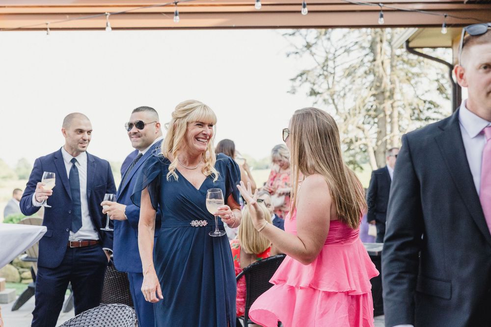 Wedding guests in navy blue and coral attire socialize during an outdoor cocktail reception.