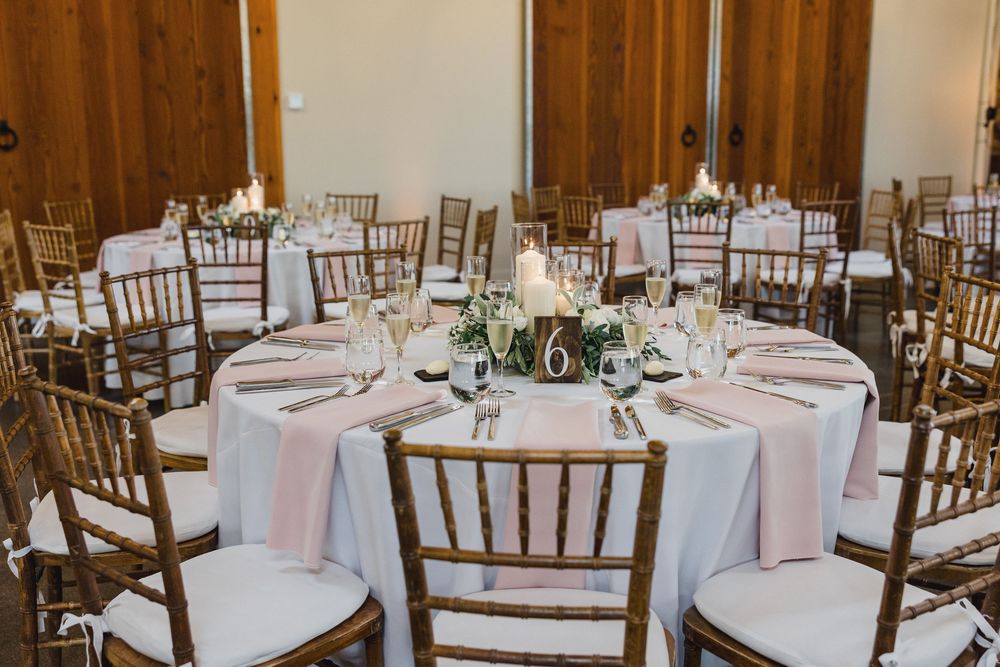 Elegant wedding reception venue with round tables set with white linens and wooden chiavari chairs.