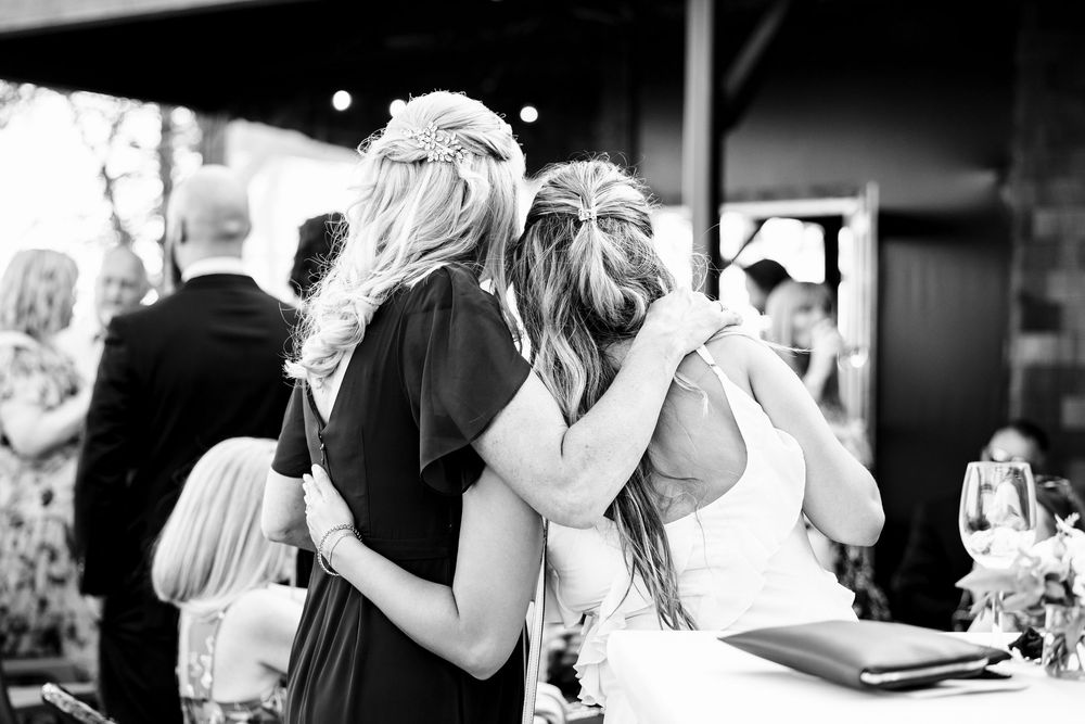 Wedding guests embrace and celebrate together at an outdoor reception in black and white.
