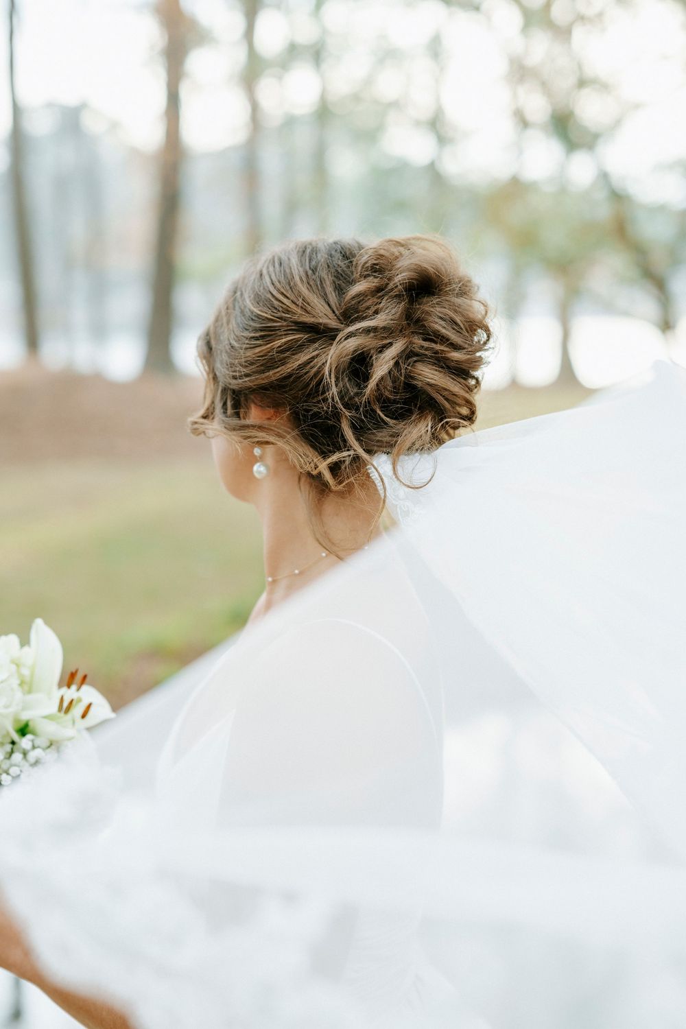 A flowing white wedding veil blows gracefully in the breeze against a soft outdoor background.
