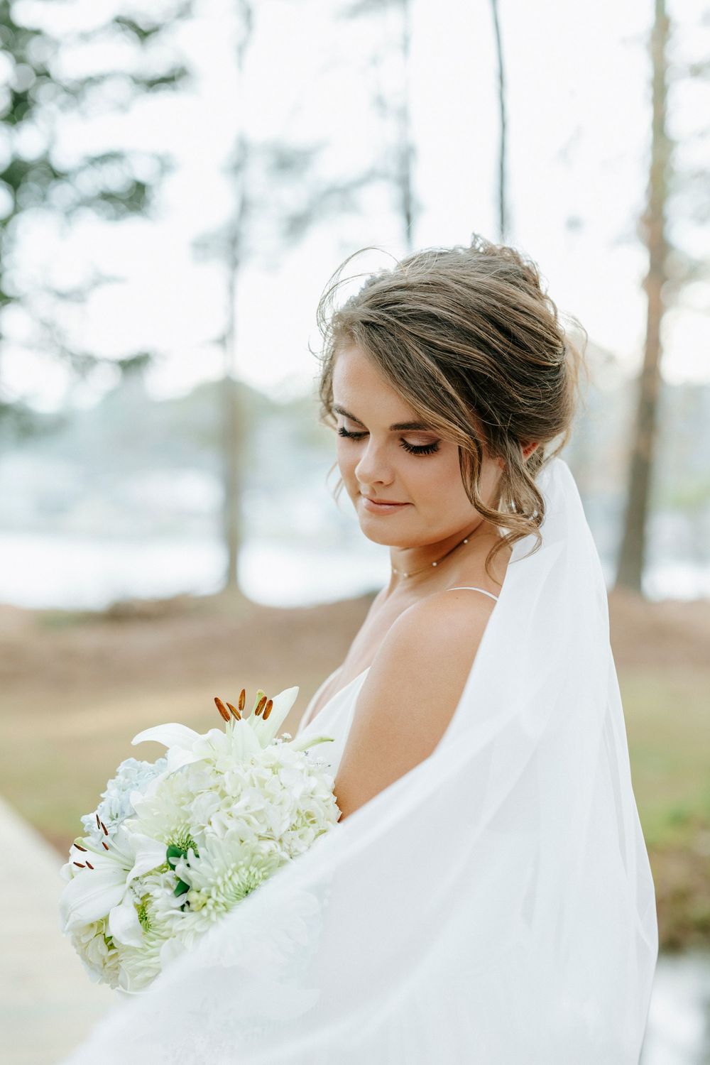 Bride in white wedding dress with veil poses in a dreamy forest setting for romantic bridal portraits.