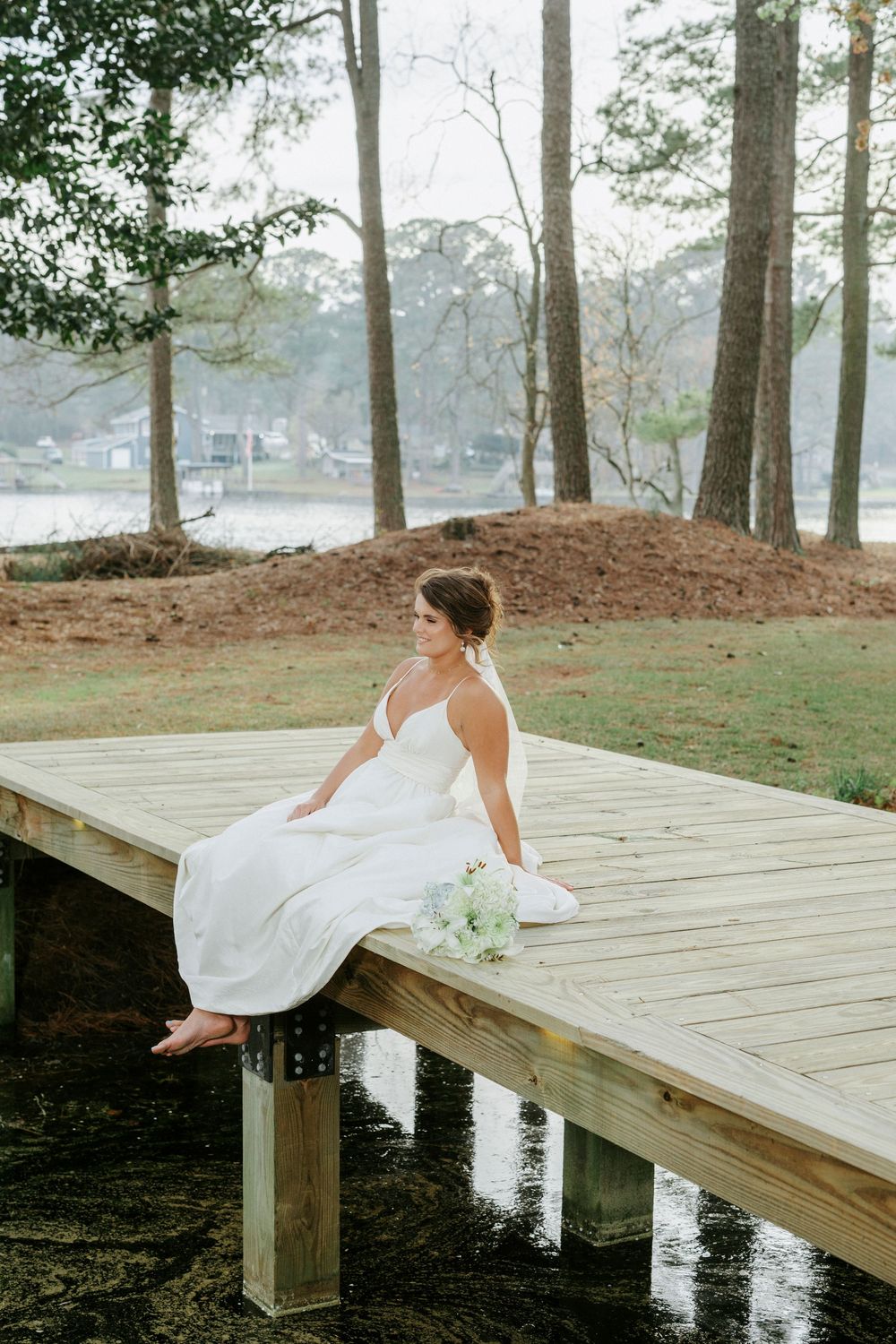 Elegant white wedding dress flowing across a wooden dock by a serene lake surrounded by trees.