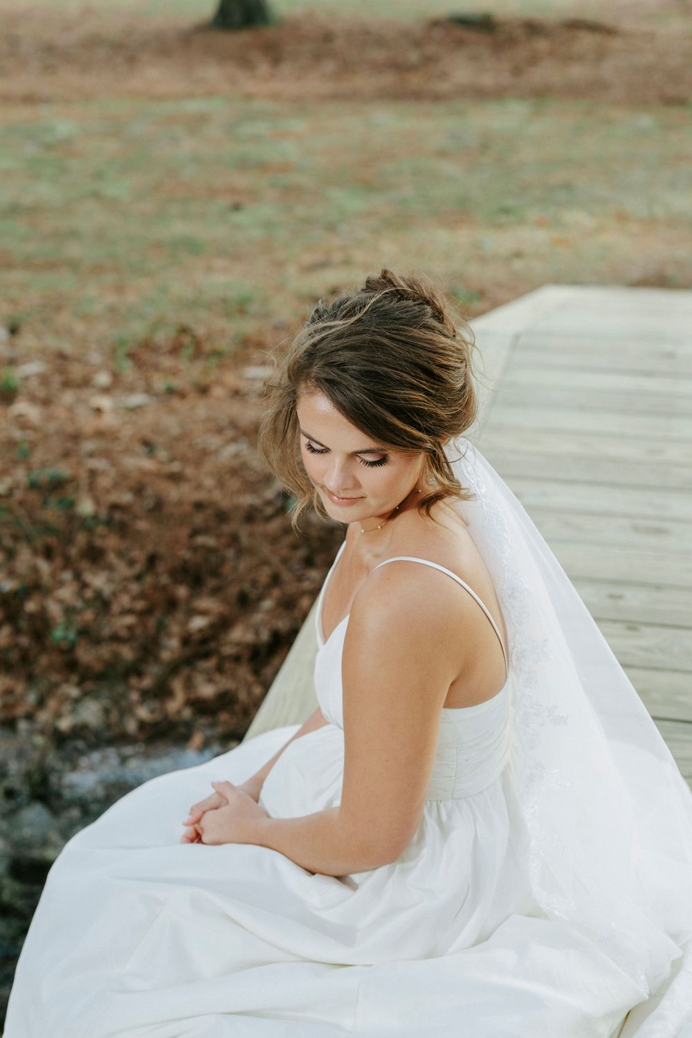 A bride in a white wedding dress poses gracefully on wooden steps surrounded by autumn leaves.