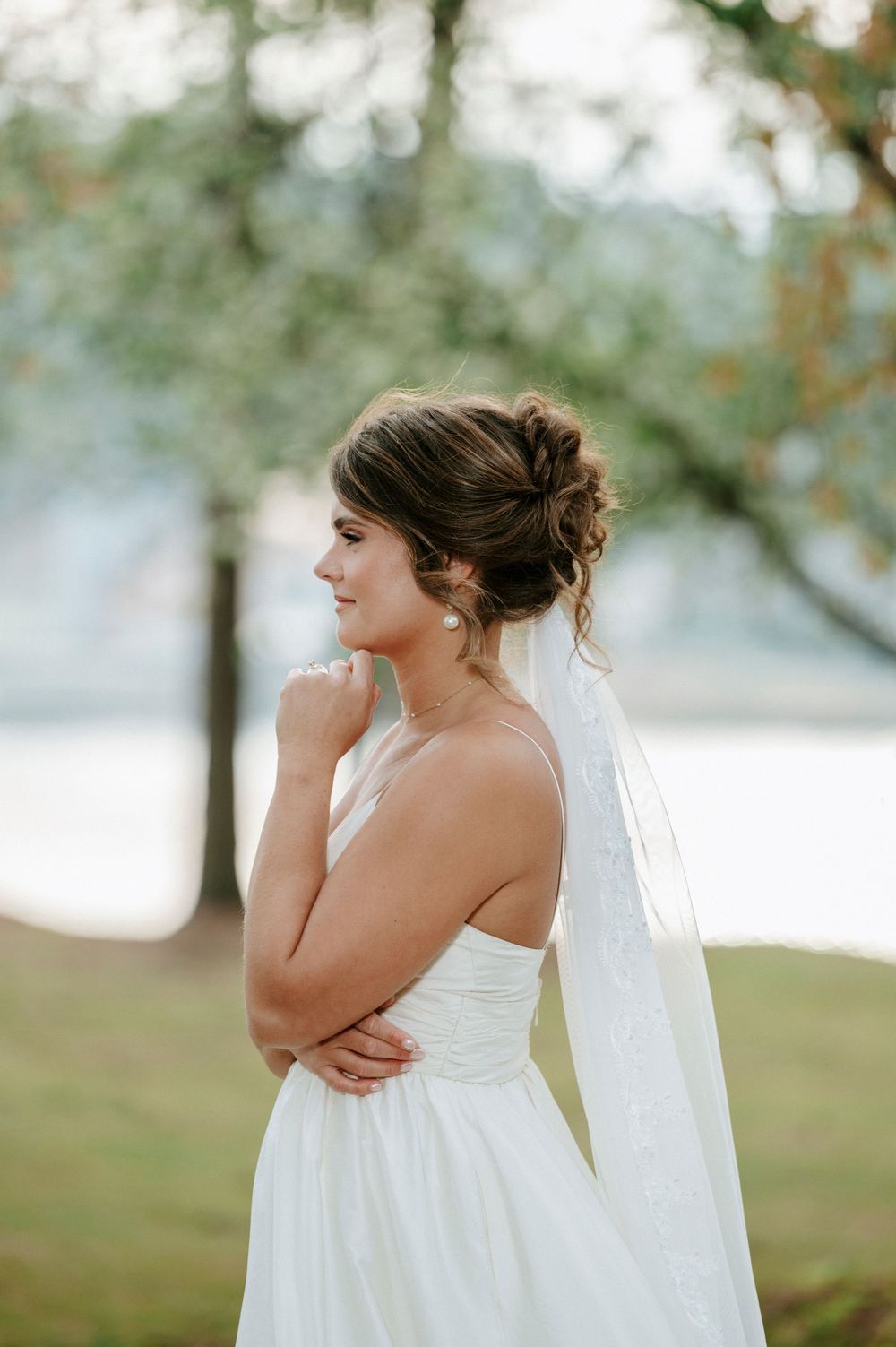 A bride in a flowing white wedding dress stands outdoors in a dreamy pose with soft natural lighting.